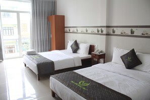 Habitación de hotel con dos camas, un armario de madera, baño con inodoro y lavamanos, y balcón con vistas a edificios.