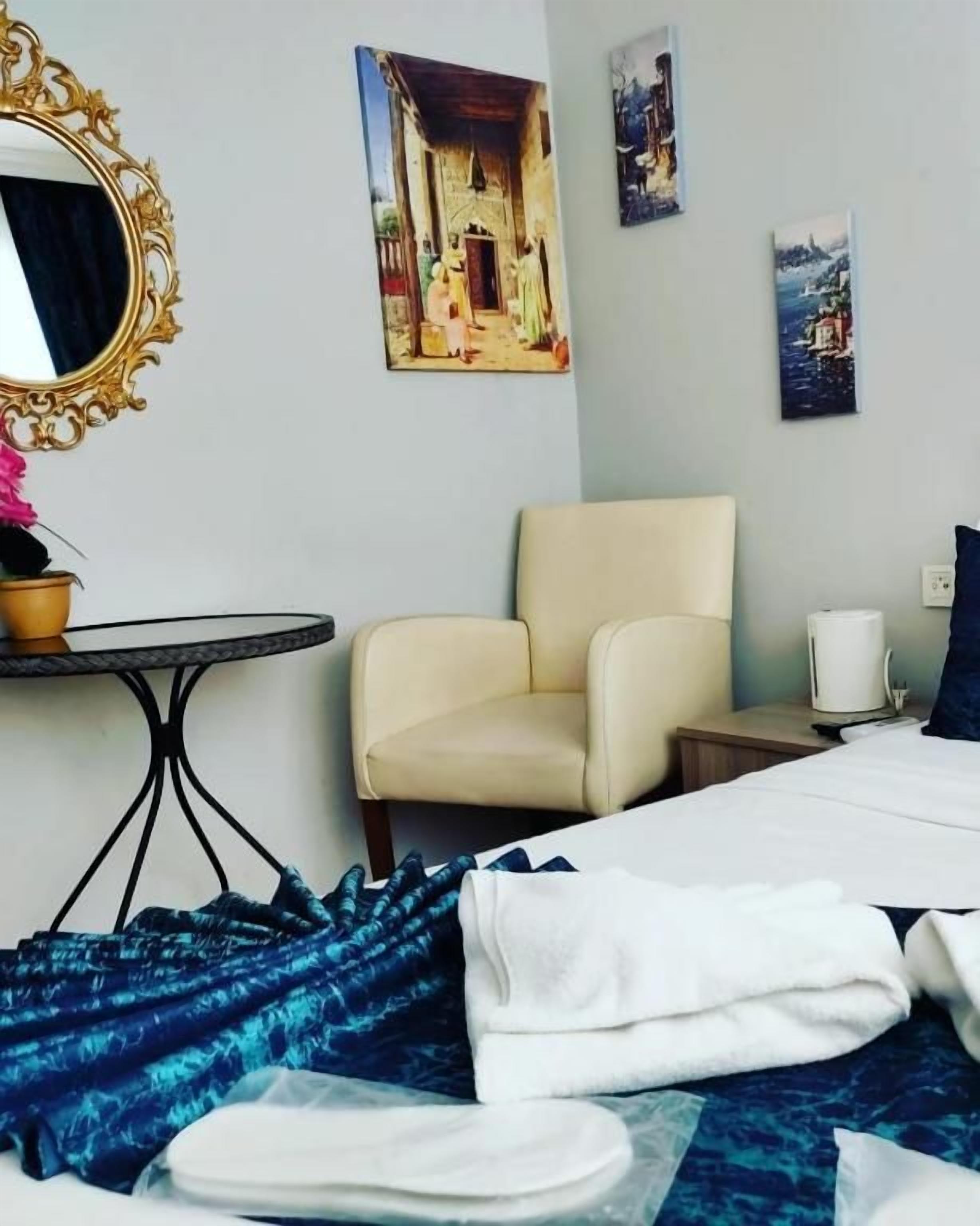A hotel room with a bed, a chair, a table, and artwork on the walls.