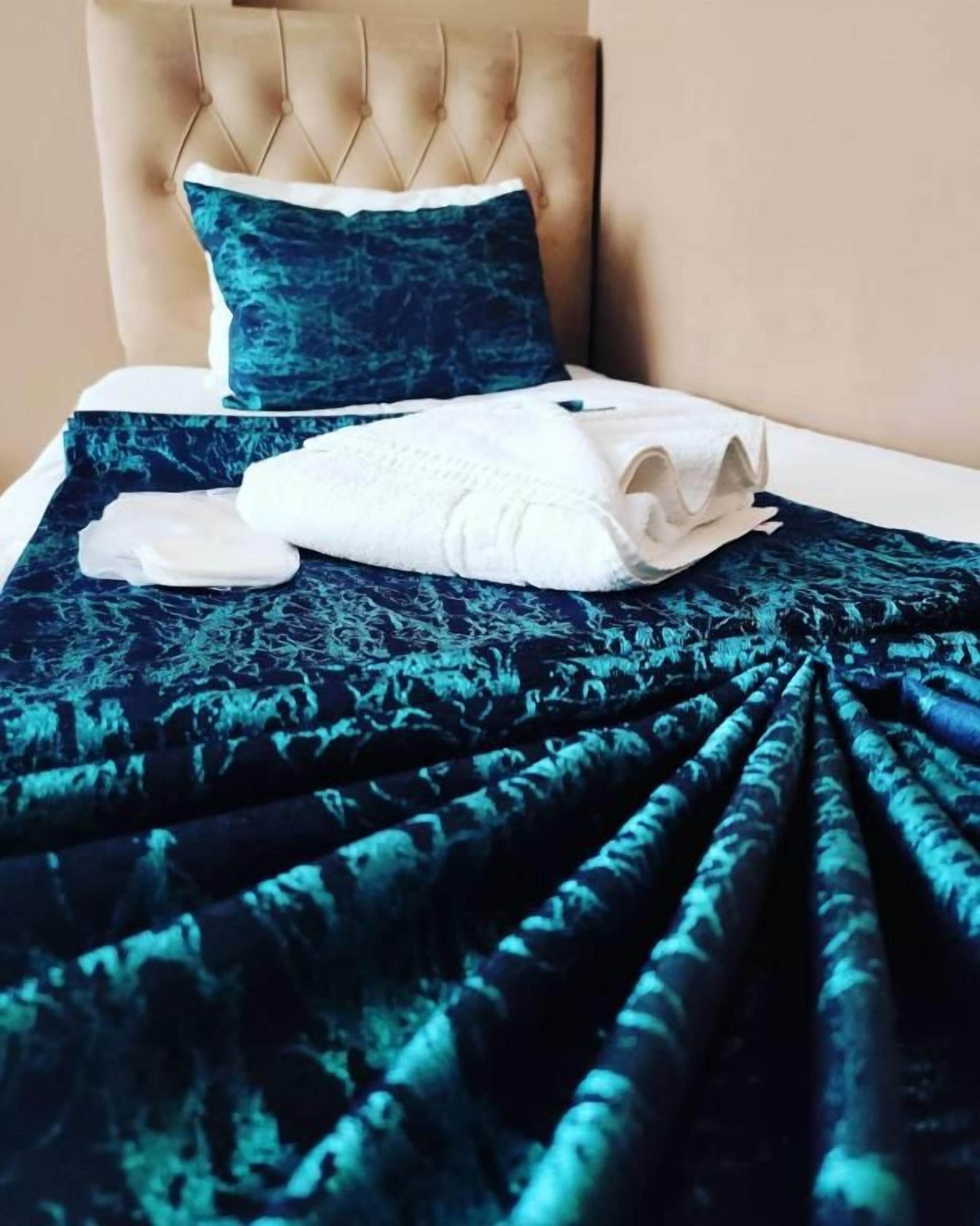 A bed with a tufted headboard, a dark blue patterned bedspread, and a white pillow.