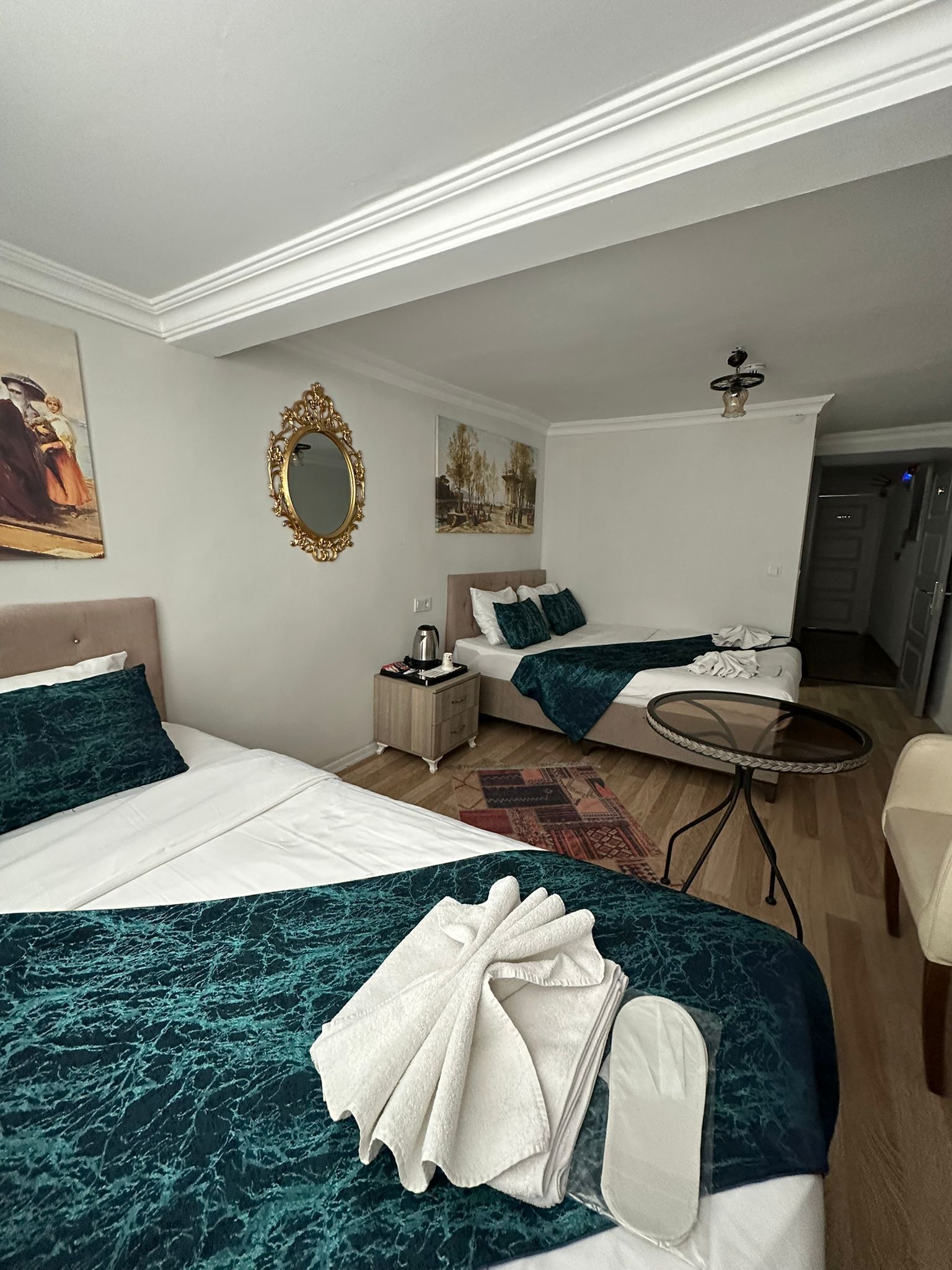 A hotel room with two beds, a round table, a mirror, and artwork on the walls.