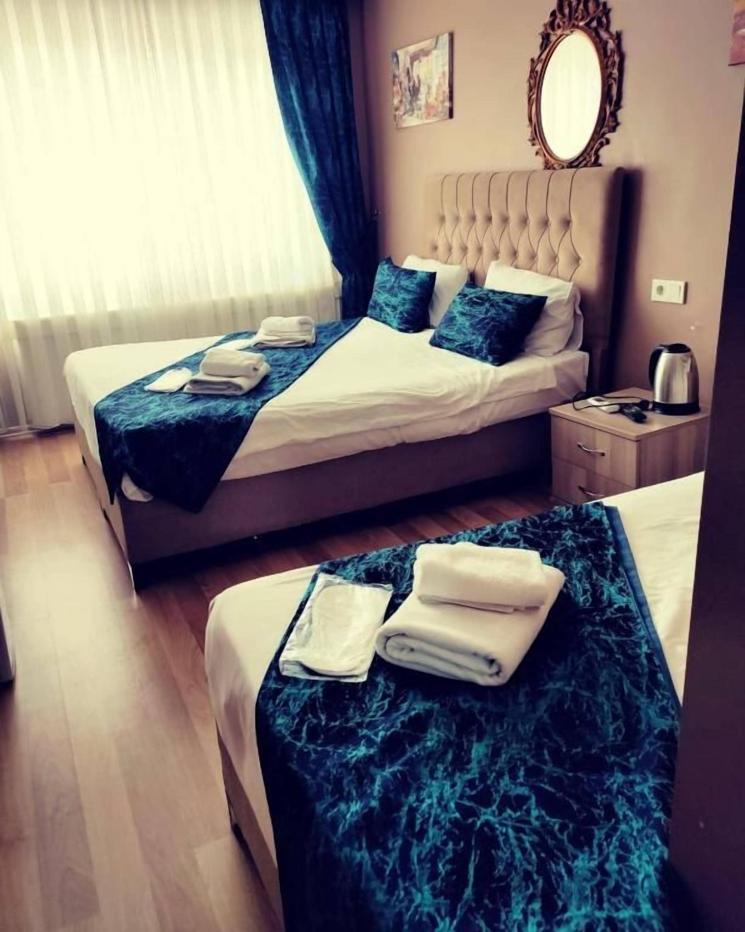 A hotel room with two beds, a bedside table, a nightstand, a mirror, and a window with curtains.