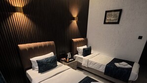 A hotel room with two beds, a wooden accent wall, a framed picture, and a nightstand with a coffee pot. - Hotel Estambul (Istanbul)