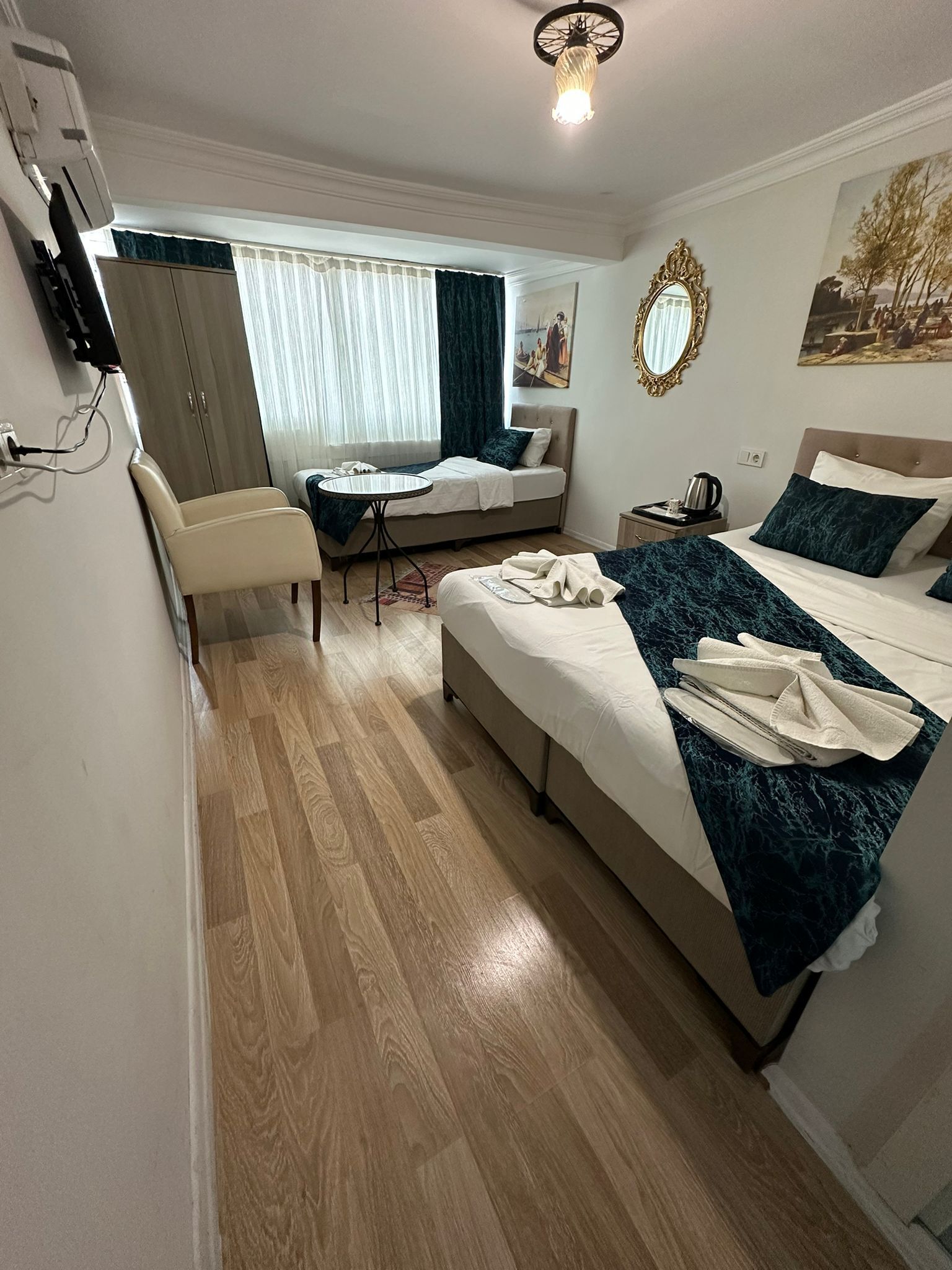 A hotel room with a bed, a desk, a chair, a bedside table, and a wall-mounted TV.