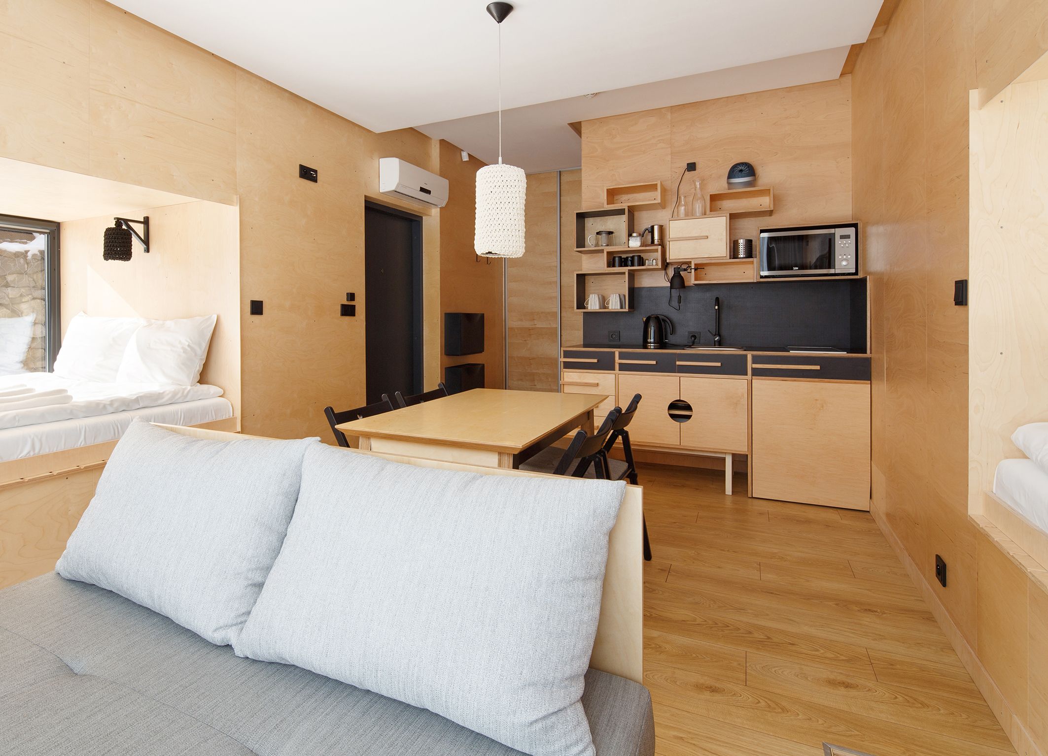 Un espace de vie compact comprenant un coin cuisine, un coin repas et un espace nuit avec un canapé et des coussins.