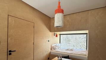 A room with a wooden door, a window seat with a view, a table with a chair, and a hanging light fixture.