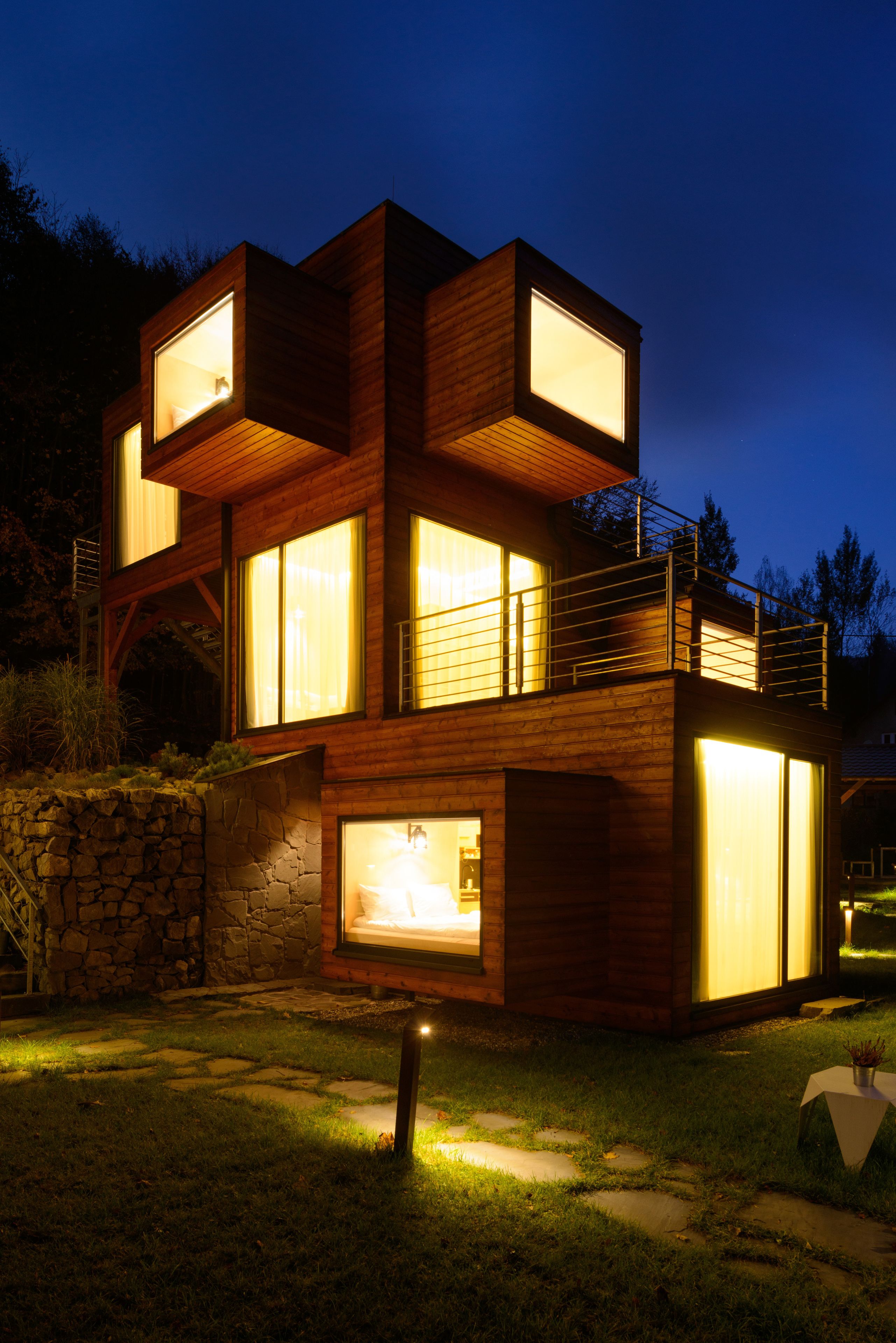 A modern two-story wooden house with large windows and a stone wall foundation.