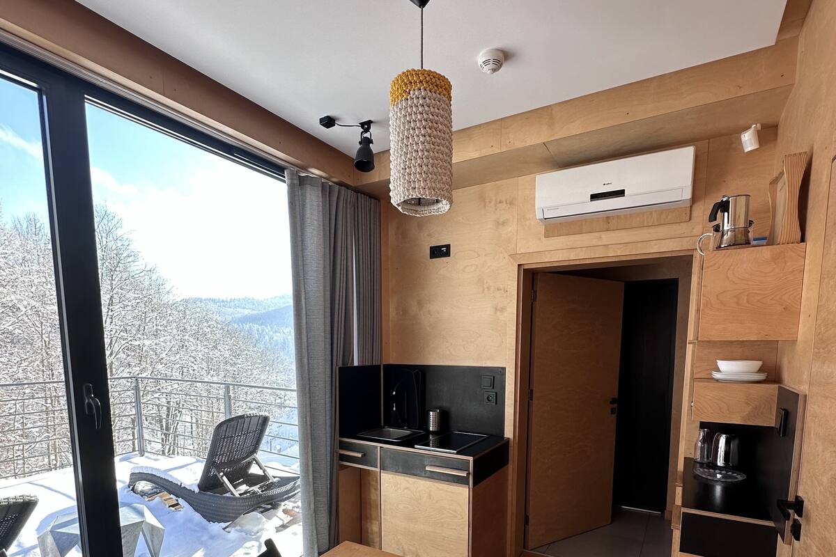 A compact kitchen with a dining area, a large window offering a view of a snowy landscape, and a built-in oven.