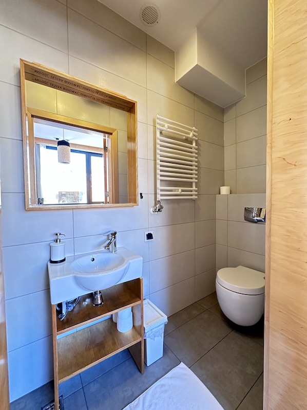 Un baño moderno con un espejo grande, lavamanos blanco y un inodoro.
