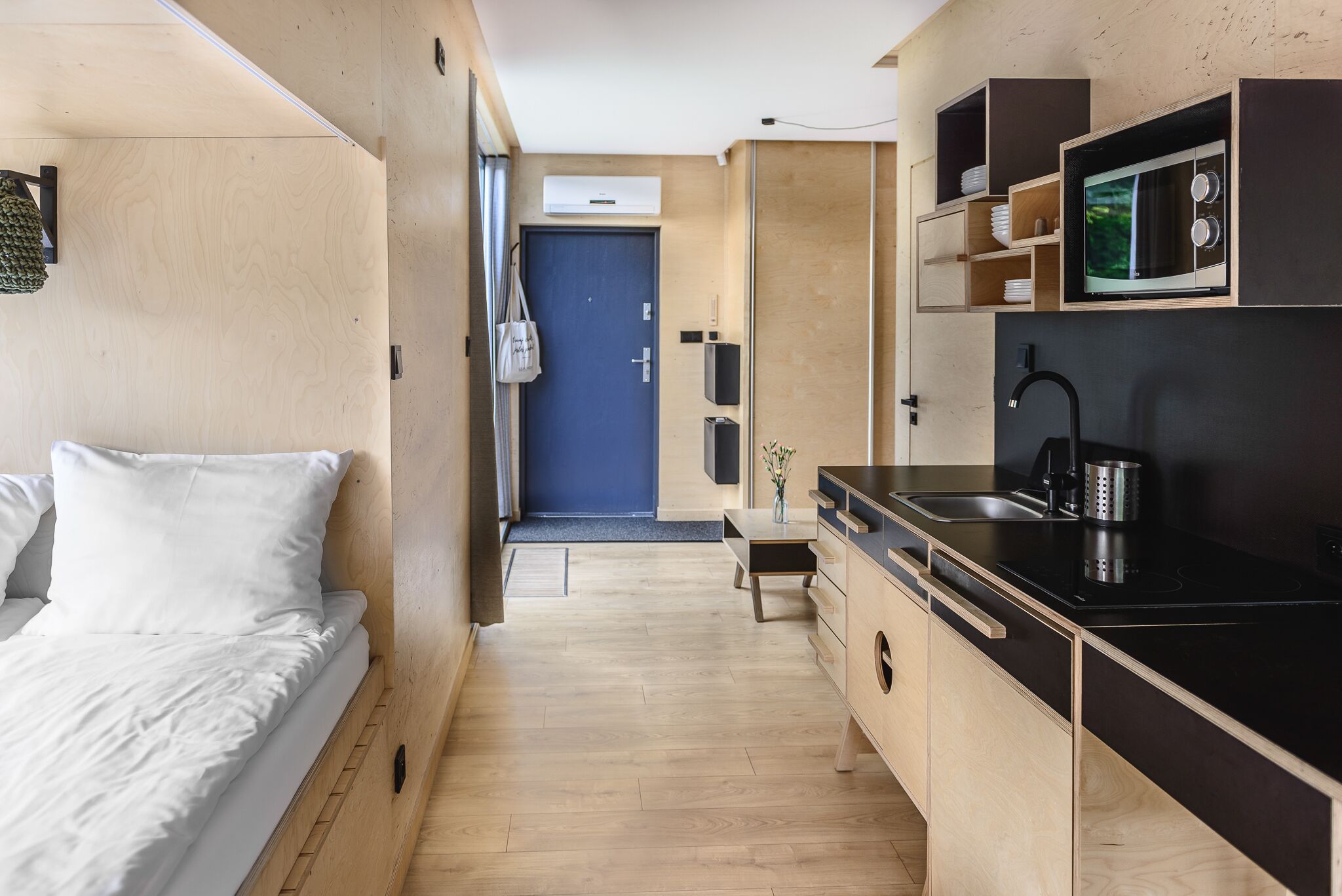 A compact hotel room with a bed, a small kitchenette, and a bathroom.