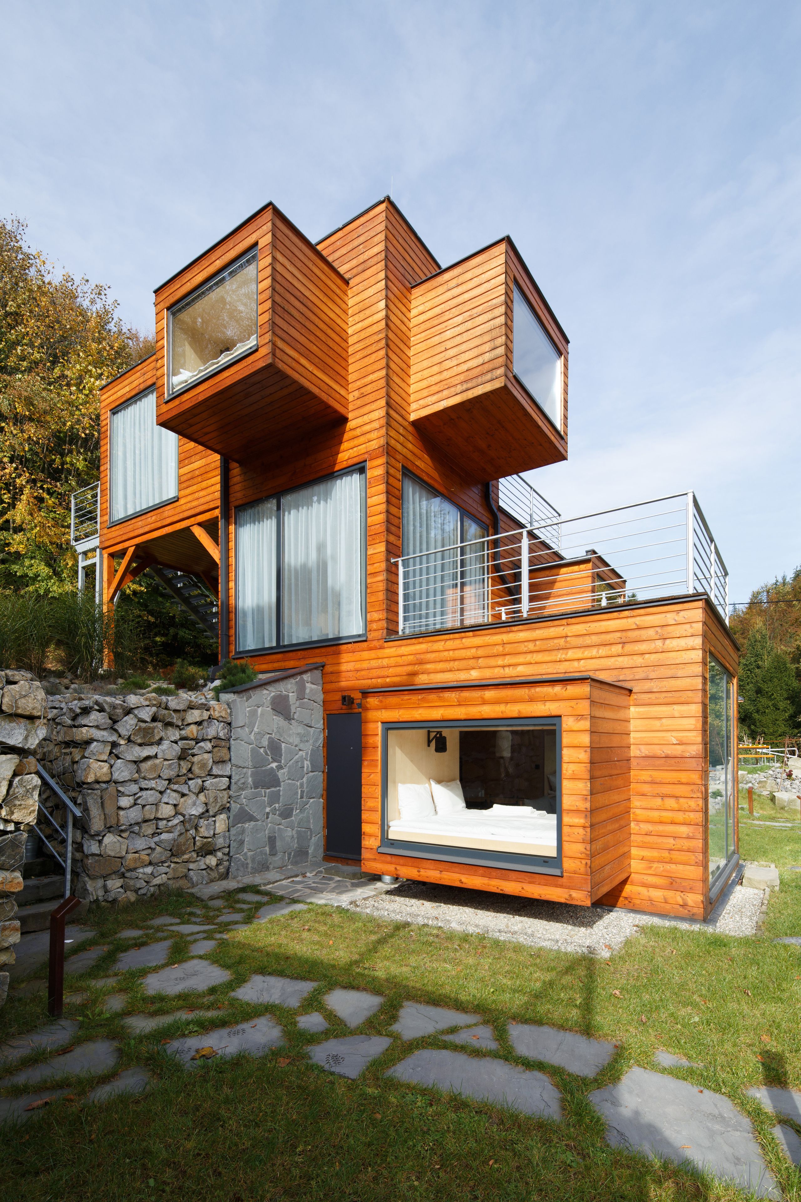 A modern multi-story house with a stone foundation, wooden exterior, and large windows.