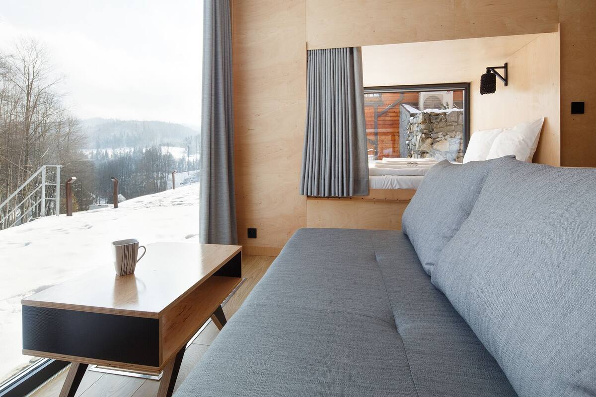 A modern room with a sofa, a table with a mug, and a window overlooking a snowy landscape.