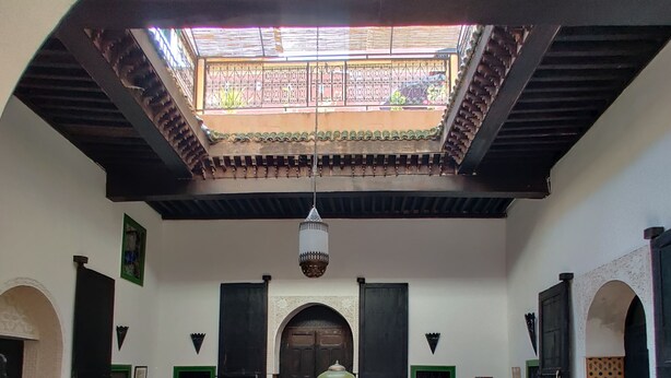 A courtyard with a tiled floor, a central table, chairs, and a hanging light fixture. - Riad Menthe Et Citron (Meknes)