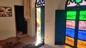 A room with a bed, a chair, a colorful stained glass window, and a door leading to a staircase. - Riad Menthe Et Citron (Meknes)