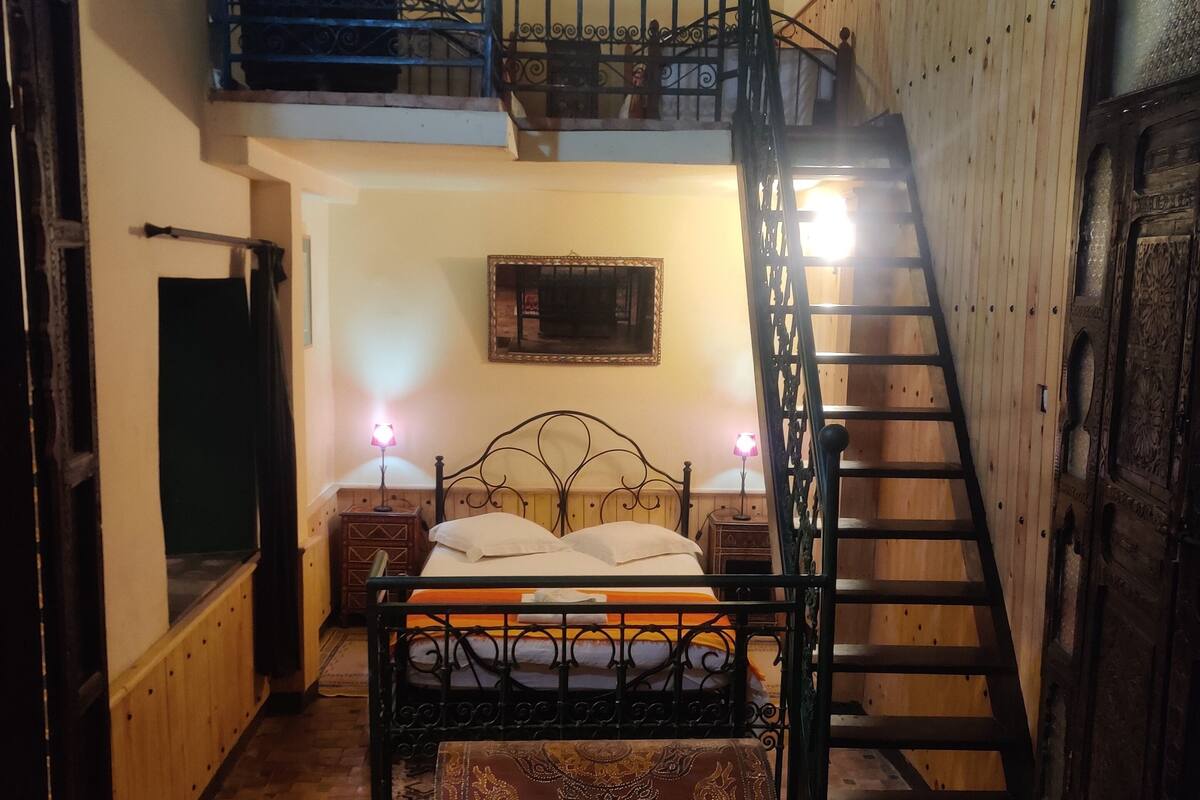 A bedroom with a bed, a wooden floor, a staircase, and a balcony.