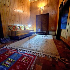 Ein Zimmer mit Holzwänden, einer Couch mit gemusterten Kissen, einem Tisch mit einem Laptop und einem großen Teppich.