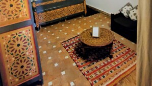 A room with a bed, a small table, a patterned rug, a decorative cabinet, and a window. - Riad Menthe Et Citron (Meknes)