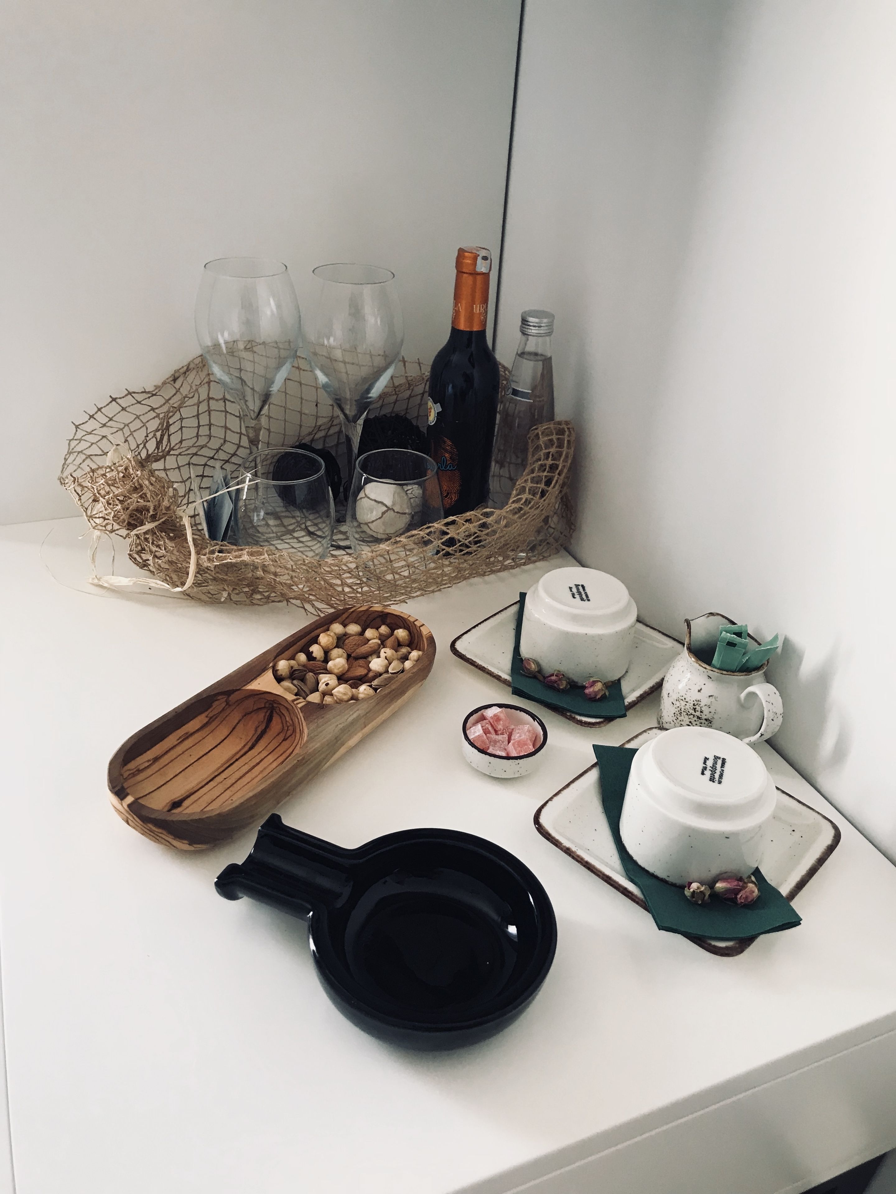 A neatly arranged table with a bottle, glasses, a wooden bowl, a small bowl of sugar cubes, and a black bowl.