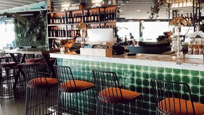 A bar area with hexagonal pendant lights, a green-tiled bar counter, and metal wire chairs with orange cushions. - Fermaki Rooms - Adults Only (Urla)