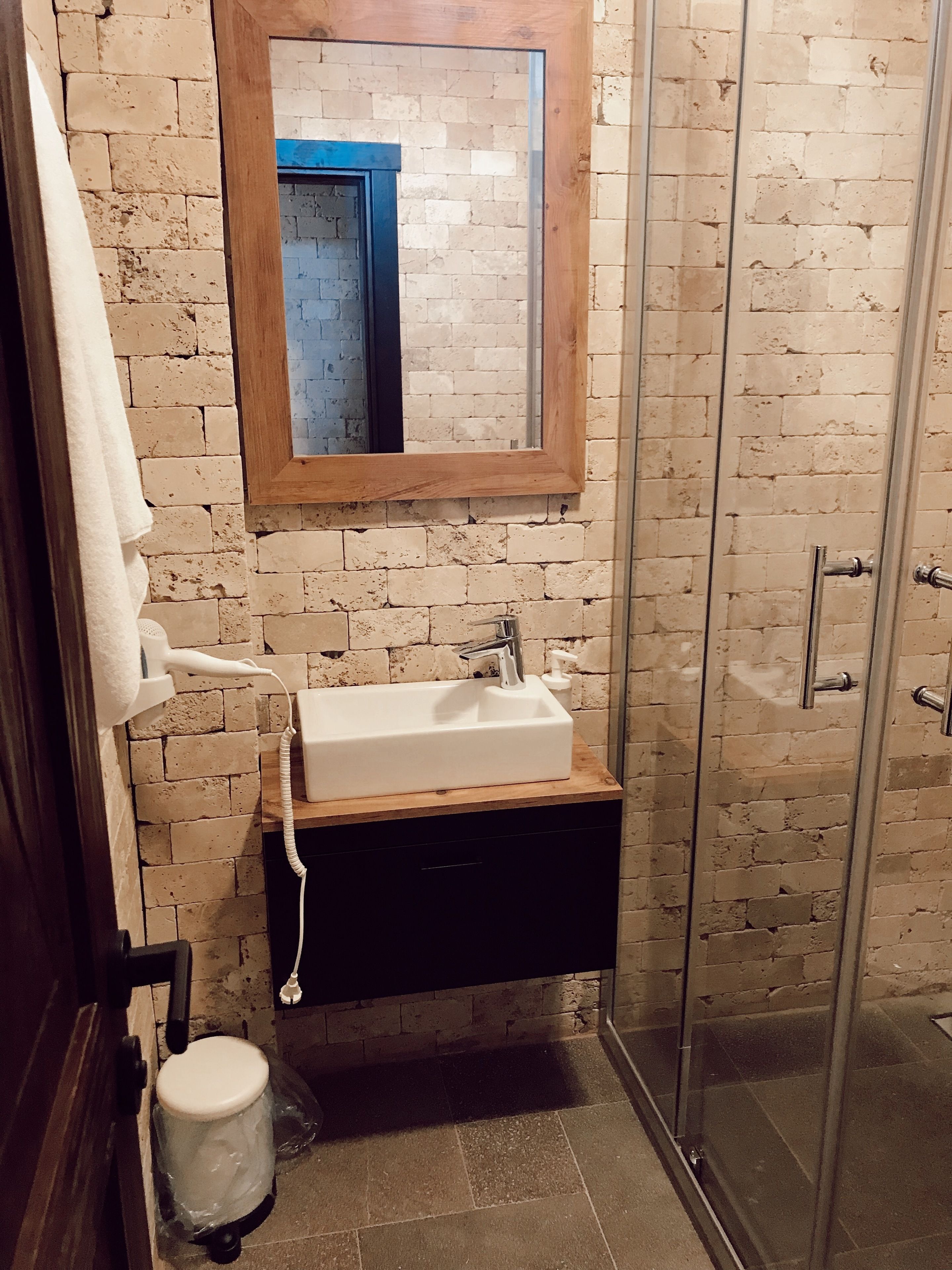 A bathroom with a white sink, a wooden medicine cabinet, a mirror, and a glass shower enclosure.