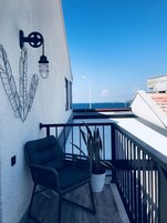 A balcony with a black chair, a potted plant, and a wall with a light fixture and decorative leaves.