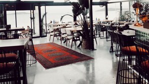A spacious restaurant with high ceilings, modern pendant lighting, and a large window overlooking a scenic view. - Fermaki Rooms - Adults Only (Urla)