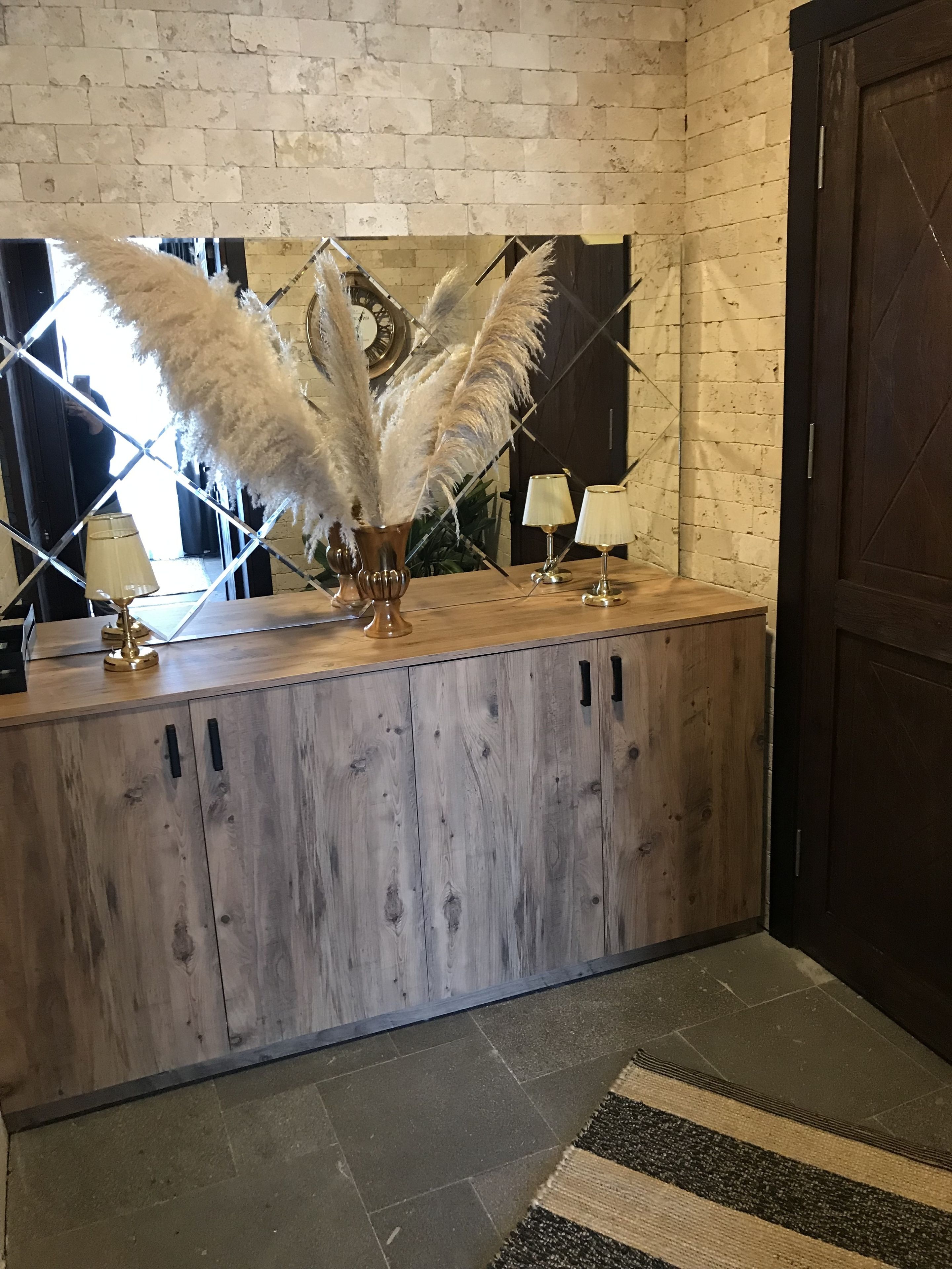 A wooden reception desk with a clock, two lamps, and a decorative plant with white feathers.