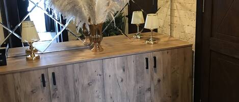 A wooden reception desk with a clock, two lamps, and a decorative plant with white feathers.