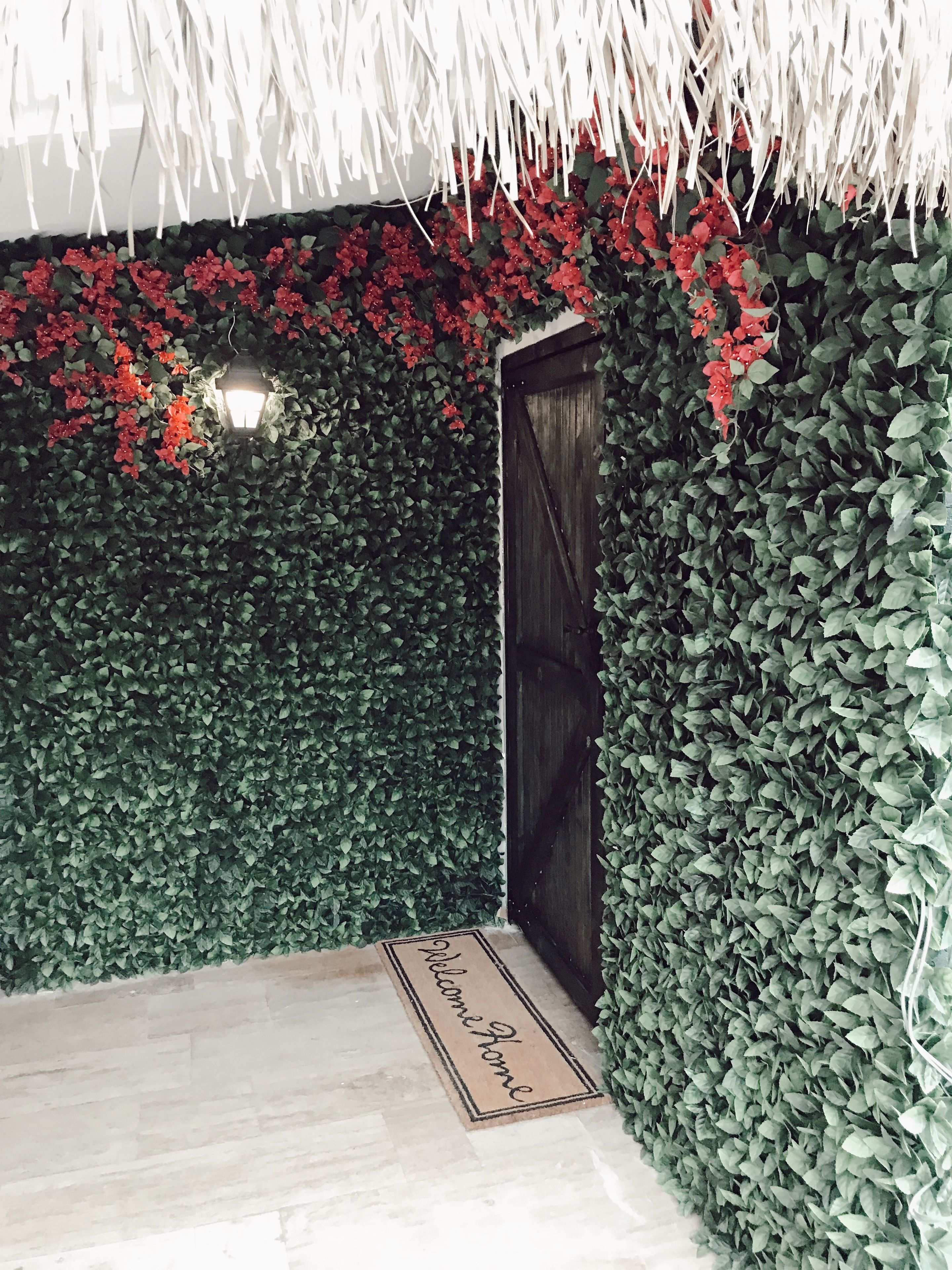 Une pièce avec une porte en bois sombre, un paillasson et un mur recouvert de feuillage vert et de fleurs rouges.