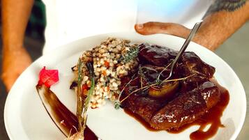 A person holding a plate with a dish of meat, grains, and vegetables, and a decorative element on the side.