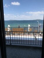 A balcony with a view of the sea, a wooden deck, and a fenced area with umbrellas.