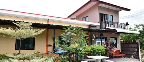 A two-story house with a balcony, a patio with a table and benches, and various plants.