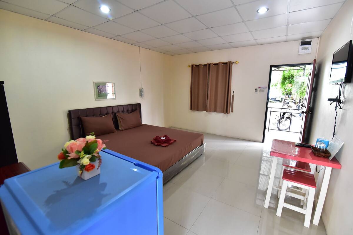 A hotel room with a bed, a desk, a chair, a small table with a vase of flowers, and a window with curtains.