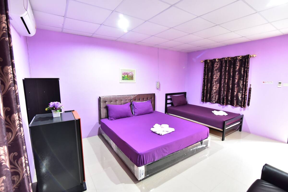 A room with two beds, each with purple bedding, a black desk, and a small potted plant.