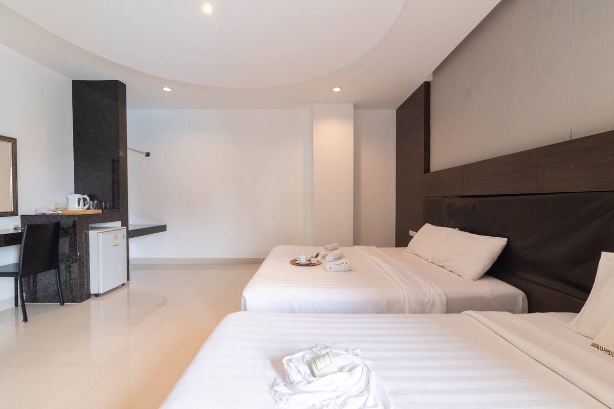Een hotelkamer met twee bedden, een bureau en een kleine kitchenette.