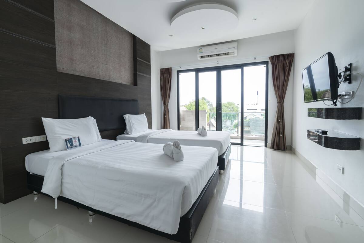 Een moderne hotelkamer met twee bedden, een flatscreen televisie en een grote schuifdeur naar het balkon.