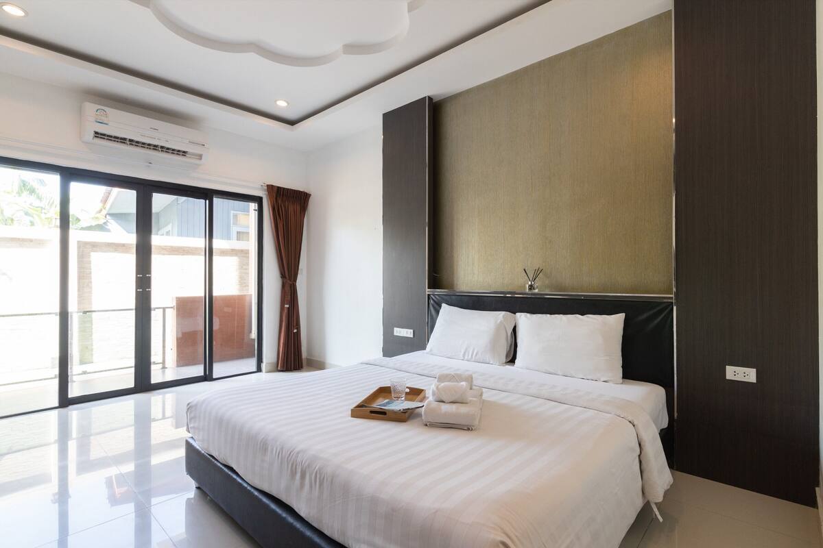 Een moderne hotelkamer met een groot bed, een nachtkastje, een dienblad met handdoeken en uitzicht door de glazen deur.