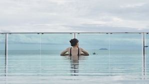 A person in a glass-bottomed infinity pool with a view of the sea and distant islands. - Tribe Pattaya (Pattaya)