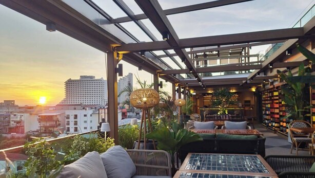 A rooftop terrace with a glass ceiling, outdoor seating, and a view of the city skyline at sunset. - Tribe Pattaya (Pattaya)