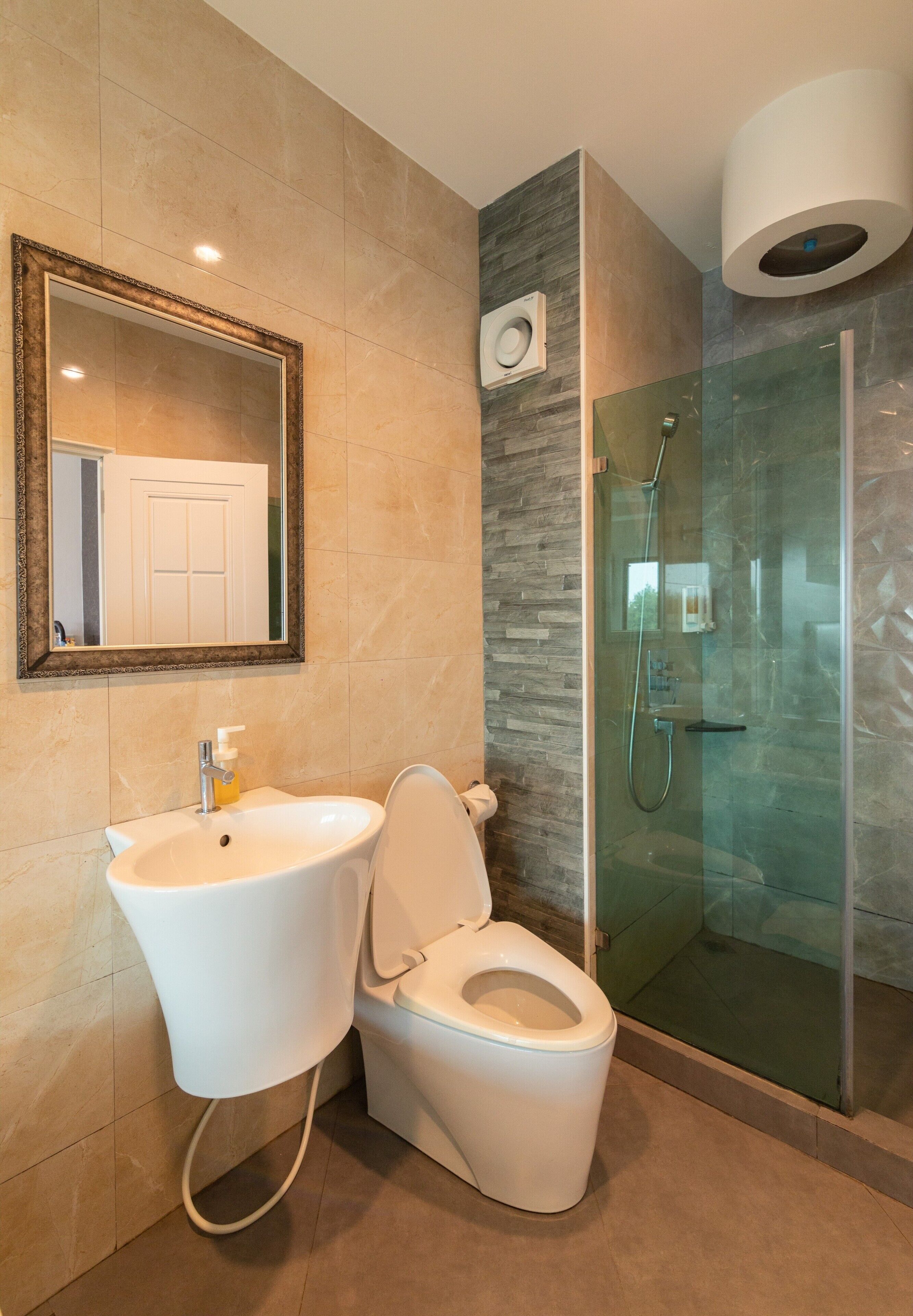 Ein modernes Badezimmer mit einer Duschkabine aus Glas, einem weißen Waschbecken mit Seifenspender und einer Toilette.