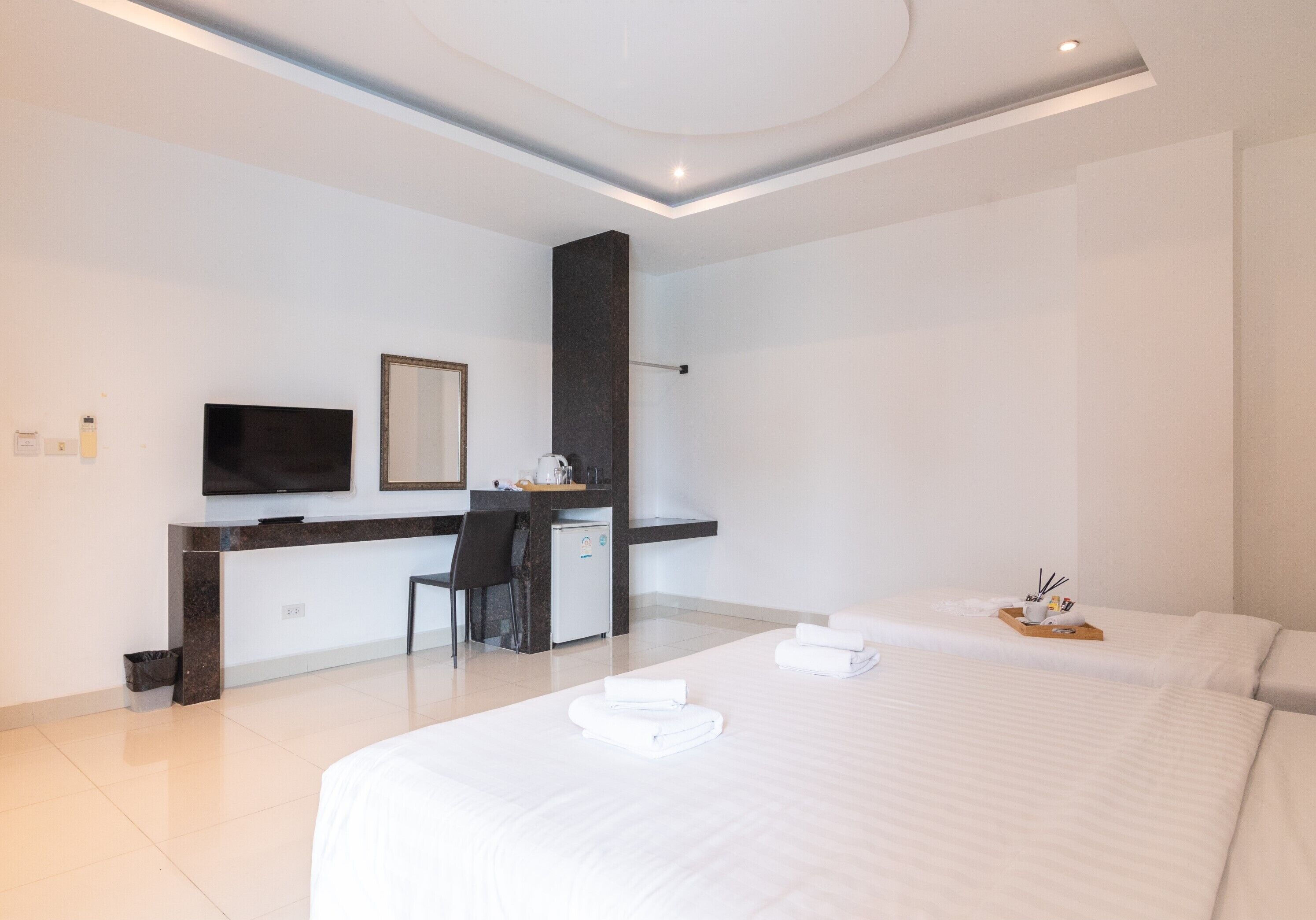 A modern hotel room with a large bed, a desk with a chair, a flat-screen TV, and a small kitchenette.