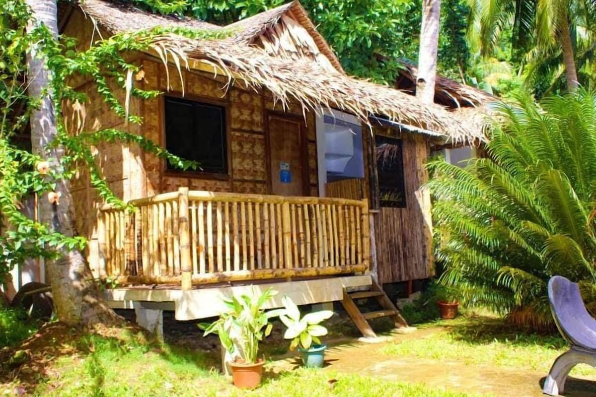 A rustic wooden house with a thatched roof, a balcony, and a small porch.
