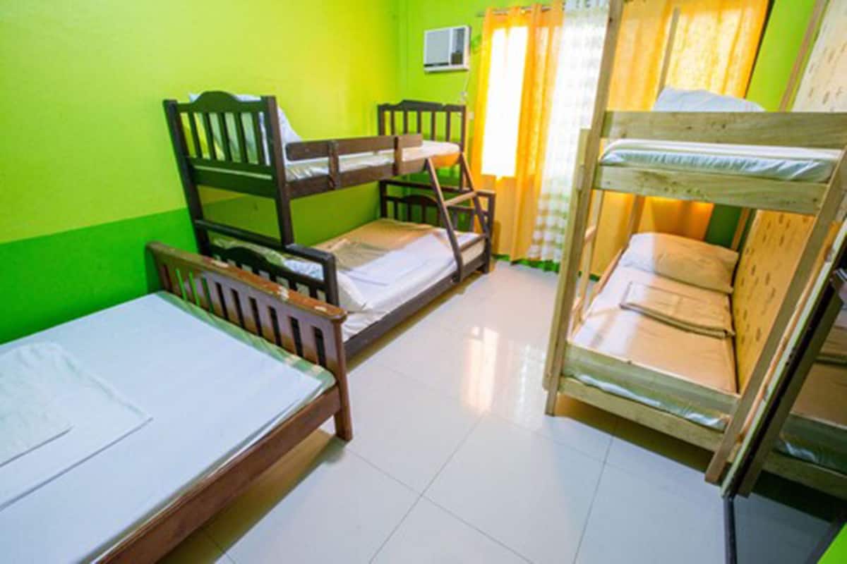 A room with bunk beds and a single bed, green walls, and a tiled floor.