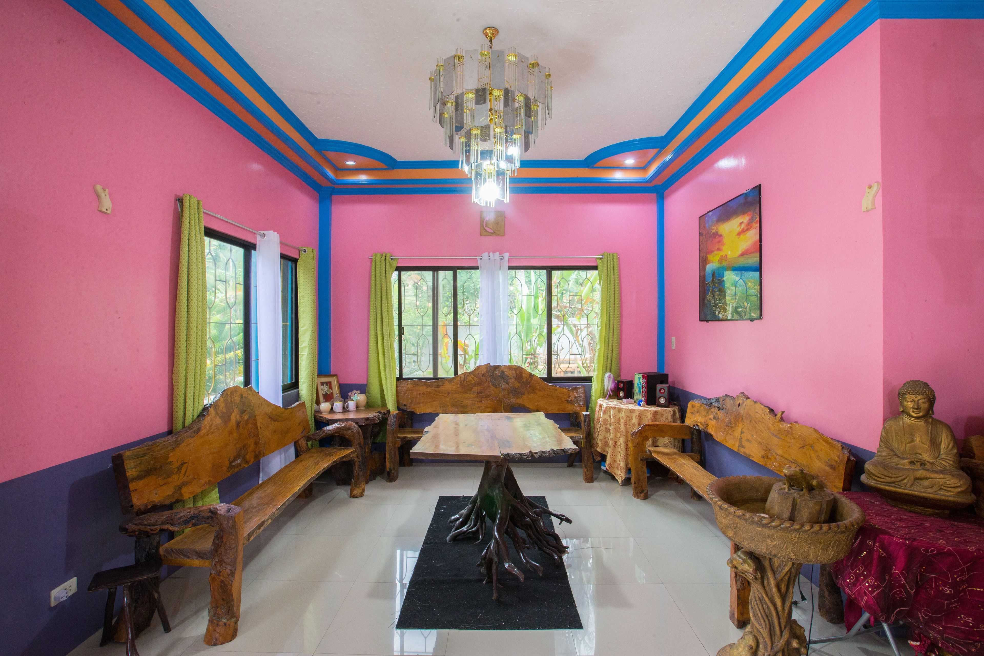A room with a wooden table, benches, a Buddha statue, and a chandelier.