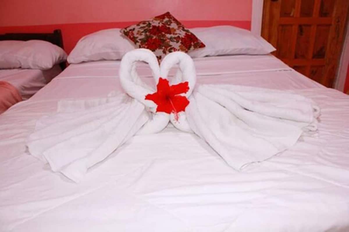 A bed with white linens and a red bow centerpiece.