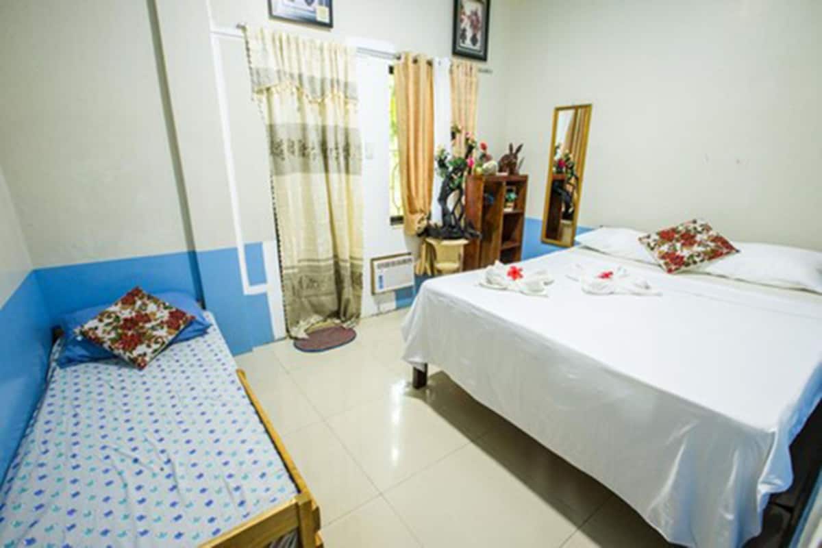 A room with a single bed, a smaller bed, a mirror, and a small table with a chair.
