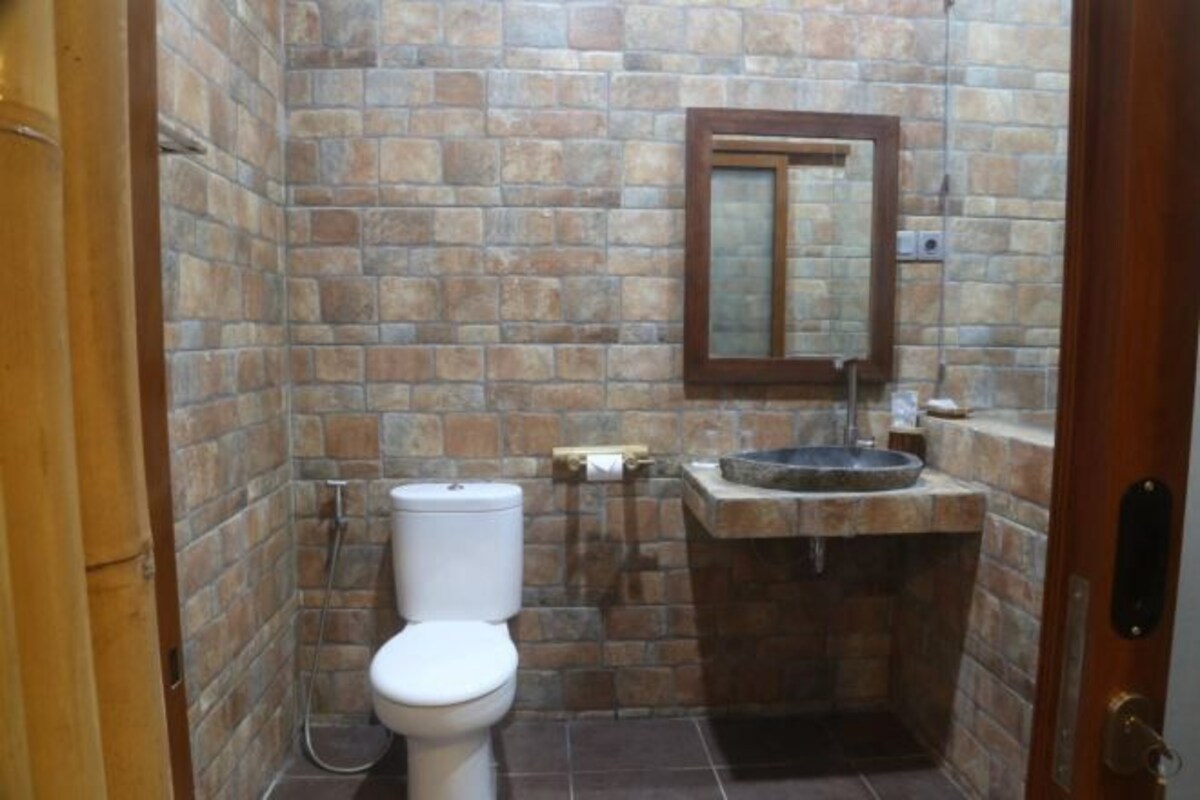A bathroom with a stone wall, a toilet, a sink, and a mirror.
