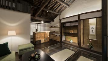 A traditional Japanese-style room with tatami flooring, a low table with a tea set, a green cushioned bench, a wooden cabinet with shelves, and a hanging scroll on the wall.
