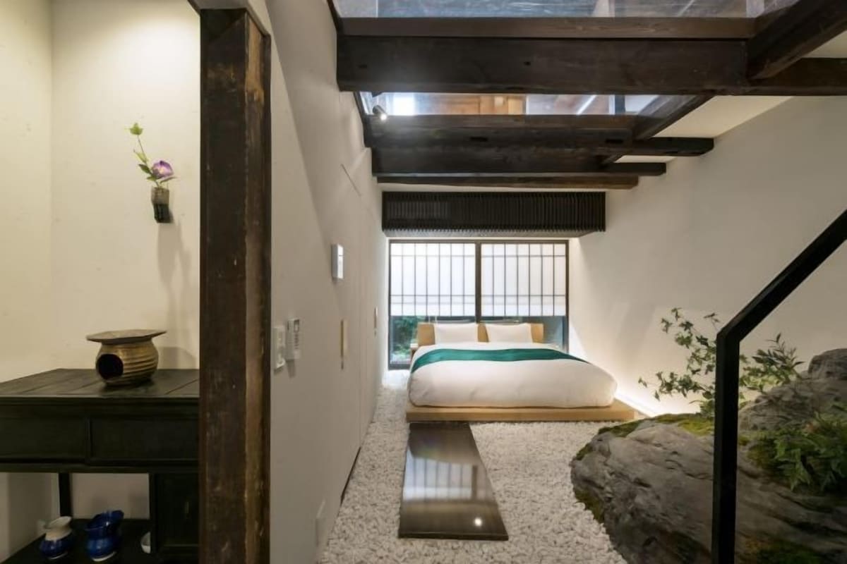 A traditional Japanese-style bedroom with tatami flooring, a low platform bed, and a sliding door leading to a view of greenery.