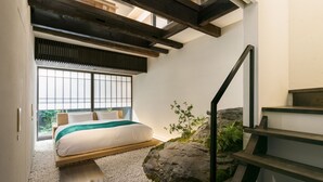 Un dormitorio con cama, vistas por una ventana, una escalera y una formación rocosa.