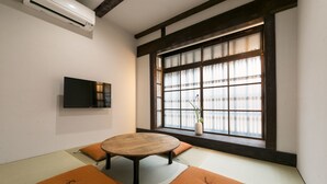 Una habitación japonesa tradicional con suelo de tatami, una mesa redonda y un televisor montado en la pared.